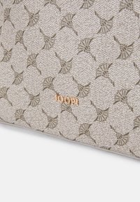Bolsa bege com uma superfície texturizada, apresentando um padrão floral repetido em verde. O nome da marca "JOOP!" está em destaque em dourado.