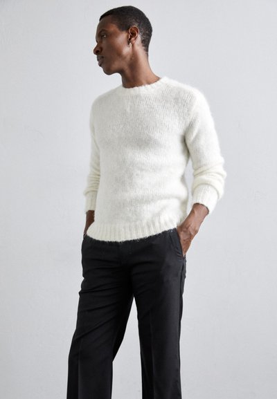 Hvid, fluffy strikket sweater med lange ærmer og rund hals, parret med sorte, skræddersyede bukser. Blød tekstur og ribbede kantdetaljer.