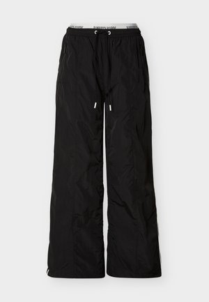 Czarne, luźne spodnie nylonowe z elastycznym pasem i sznurkiem, zamykanymi na zamek błyskawiczny bocznymi kieszeniami oraz widoczną wewnętrzną taśmą z logo Tommy Jeans.