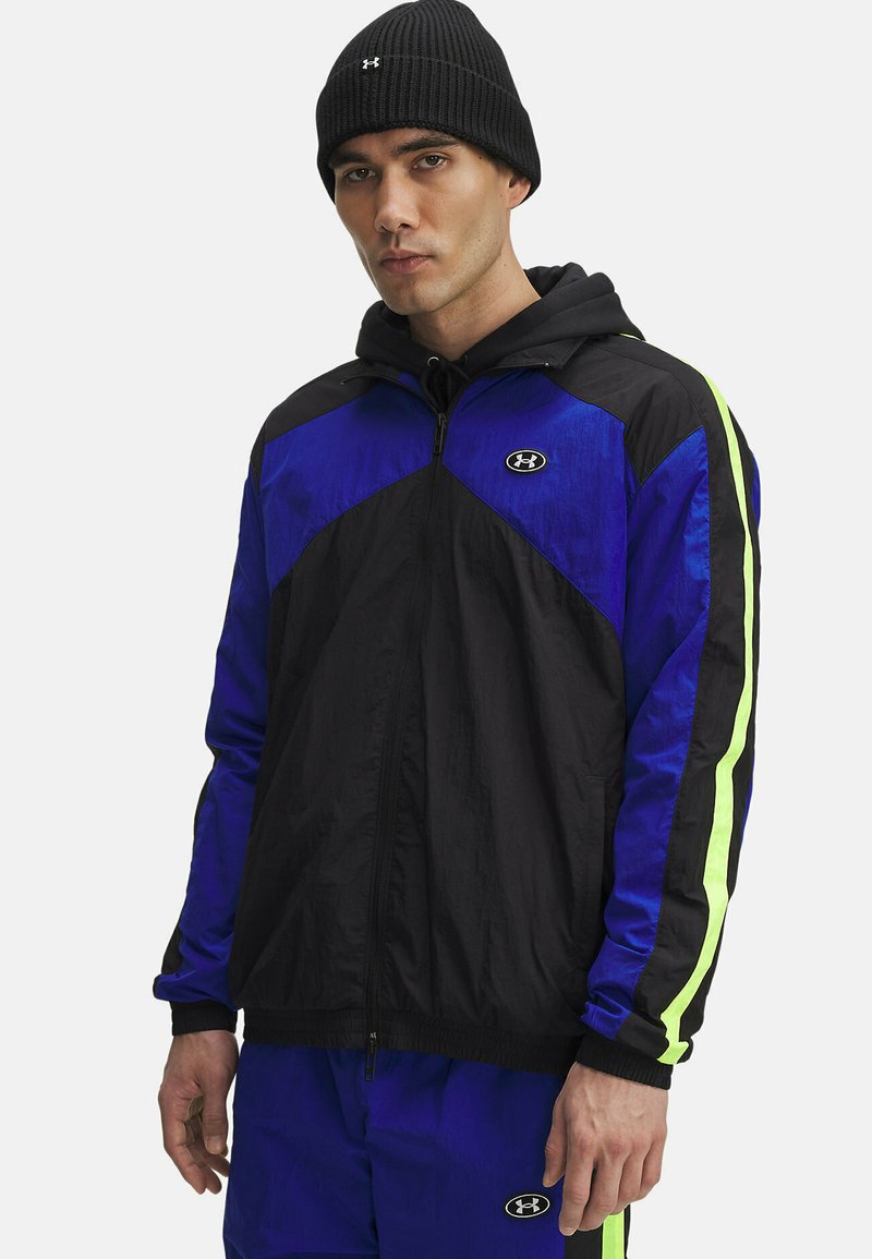 Zwarte en blauwe windjack met capuchon, met neon groene accenten op de mouwen, gemaakt van lichtgewicht stof. Inclusief rits aan de voorkant en logo.
