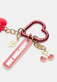 Portachiavi con un gancio metallico rosso a forma di cuore, dotato di un'etichetta rosa con la scritta "MY MELODY", un ciondolo con logo dorato e un ciondolo a forma di ciliegie.