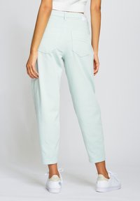 Světlé mátově zelené kalhoty s vysokým pasem a zúženými nohavicemi, se dvěma zadními kapsami a hladkou texturou, spárované s bílými teniskami.