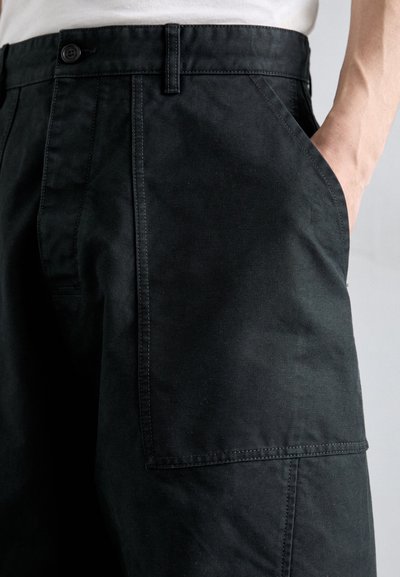 Black cargo pants made from durable fabric, featuring side pockets, a zipper closure, and a straight-leg design with visible stitching details.