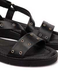 Sandales en cuir noir avec des brides croisées, des œillets en métal et une semelle rembourrée. Présente une surface texturée et une semelle durable.