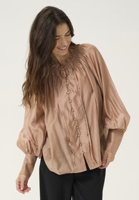 Blusa a maniche lunghe in morbido tessuto rosa chiaro con scollatura arricciata, chiusura a bottoni e maniche a sbuffo; vestibilità morbida con leggero lucido.