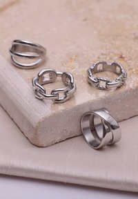Vier zilveren ringen tentoongesteld op een gestructureerd oppervlak. Kenmerken zijn onder andere gladde afwerkingen, draaien en met elkaar verbonden kettingontwerpen.
