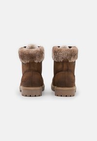 Bottines en suede marron avec un revers en fausse fourrure texturée. Elles présentent une semelle en caoutchouc robuste avec un motif de crantage. La marque est visible sur le côté.