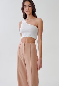 Bela enoramna cropped majica z enim ramenom z nabrano teksturo in volanskimi robovi, v kombinaciji s svetlo roza high-waisted hlačami z sprednjim šivom.