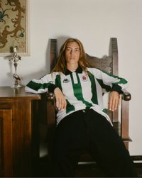 Personne aux longs cheveux assise sur une chaise en bois portant un maillot de sport rayé vert et blanc à côté d'une table en bois avec un chandelier argenté.