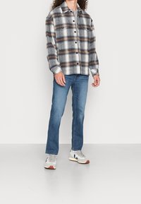 Kostkovaná košile na knoflíky v odstínech šedé, modré a oranžové; doplněná modrými džínami a šedými teniskami; má dlouhé rukávy a přední kapsy.