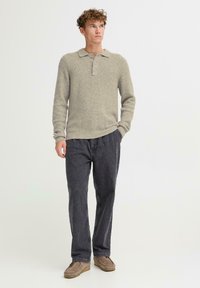 Light grey knit pullover with a collar and three buttons, paired with dark grey relaxed-fit pants and brown suede shoes. Smooth texture.