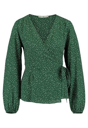 Blusa cruzada de manga larga verde con lunares blancos, escote en V, puños fruncidos y lazo lateral en la cintura.