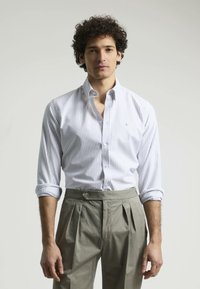 Camisa de vestir a rayas blanca y azul claro con cuello puntiagudo, botonadura frontal y mangas remangadas, combinada con pantalones gris claro con pliegues.