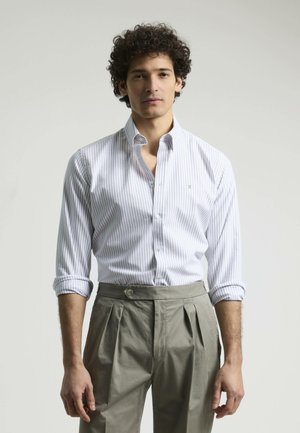Camisa de vestir a rayas blanca y azul claro con cuello puntiagudo, botonadura frontal y mangas remangadas, combinada con pantalones gris claro con pliegues.