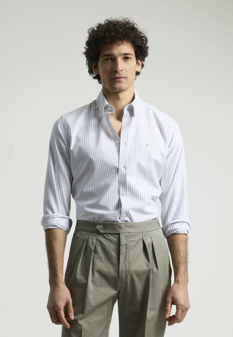 Camisa de vestir a rayas blanca y azul claro con cuello puntiagudo, botonadura frontal y mangas remangadas, combinada con pantalones gris claro con pliegues.
