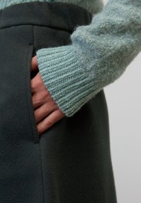 Falda de lana oscura con un bolsillo lateral; combinada con un suéter de punto texturizado en azul claro con puños acanalados.