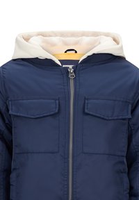 Dunkelblaue Jacke mit weißer Kapuze, ausgestattet mit zwei Brusttaschen, silbernem Reißverschluss und einem weichen Innenfutter. Das Design ist schlicht und funktional.