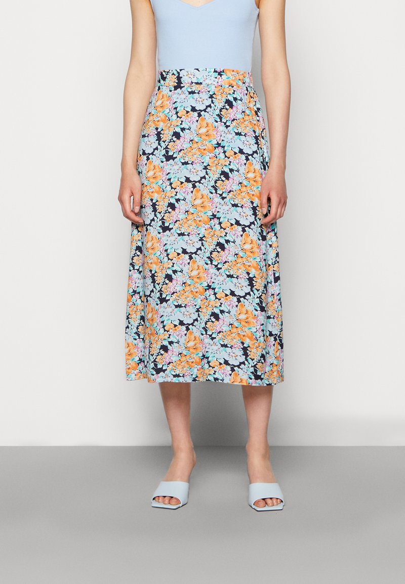 Saia midi floral com flores laranja e azul claro sobre um fundo azul marinho, combinada com uma blusa azul clara e sandálias azuis de slide.