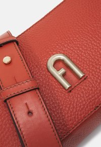 Borsa in pelle rossa con superficie a ciottoli, logo in metallo dorato, forma rettangolare e dettagli cuciti; presenta una chiusura a fibbia e a scatto.