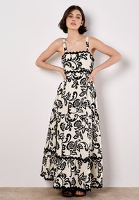 Robe maxi florale avec des motifs noirs sur fond crème, dotée de bretelles réglables et d'une jupe à volants avec des bords en feston.