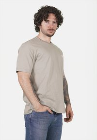T-shirt beige a maniche corte in una vestibilità rilassata, realizzato in cotone morbido con scollo rotondo e piccolo logo bianco sul petto.