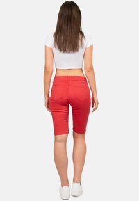 Rode denim bermuda shorts met een aansluitend ontwerp, opgerolde zoom en achterzakken. Gecombineerd met een wit cropped top en witte sneakers.