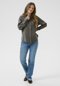 Camicia a maniche lunghe, con bottoni, in lino grigio scuro, abbinata a jeans blu e ballerine nere. Presenta un colletto e una vestibilità comoda.