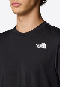 Camiseta negra de manga corta hecha de tejido suave, con un logo blanco en el lado izquierdo del pecho. Cuello redondo y diseño minimalista.