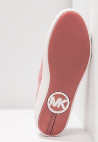 Semelle de chaussure rose avec fond en caoutchouc texturé et logo blanc "MK" près du talon, sur fond blanc.
