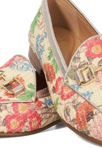 Des mocassins fleuris avec une texture tissée présentent un motif de fleurs multicolores, des bords argentés métalliques et un accent en matériel doré.