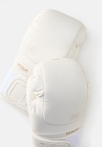 Luvas de boxe brancas com superfície texturizada, apresentando costura em tom claro de bege e números em relevo. A marca VENUM é visível.