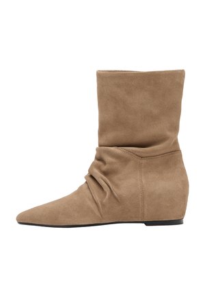 Botte en daim marron clair mi-mollet avec un design décontracté, bout pointu et semelle noire plate, vue de profil sur fond blanc.