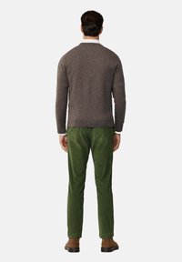 Maglione di lana grigio, design aderente, scollo rotondo. Pantaloni in velluto a coste verde, gamba affusolata. Scarpe in suede marroni. Colori semplici e solidi, senza fantasie.