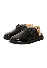 Zapatos de charol negros sin cordones con una correa ajustable con hebilla, plantilla texturizada y suela de goma gruesa con un patrón de tacos.