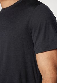 Schwarzes Rundhals-T-Shirt aus weichem Stoff, mit einer subtilen Textur und kurzen Ärmeln. Nahaufnahme des Schulter- und Armbereichs sichtbar.