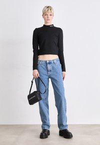 Top nero a maniche lunghe cropped con logo, jeans alta vita blu chiaro, borsa a spalla nera e scarpe platform nere chunky.