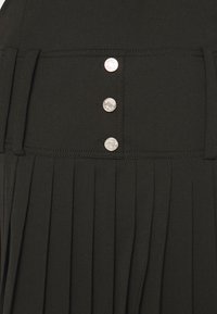 Μαύρη πλισέ φούστα με φαρδύ λάστιχο που διαθέτει τρία μεταλλικά κουμπιά. Το ύφασμα έχει λεία υφή με καλοφτιαγμένες πτυχές για ευκολία στην κίνηση.