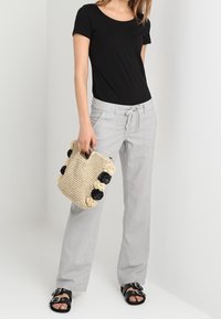 Czarna bluzka z krótkim rękawem, jasnoszare luźne spodnie z sznurkiem, pleciona beżowa torba z czarnymi kwiatowymi akcentami oraz czarne sandały na klamry.