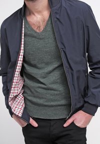 Granatowa kurtka bombowca z zapięciem na zamek, z wcheckered czerwono-białą podszewką. Noszona na zielonym swetrze z dekoltem w serek i czarnych spodniach.