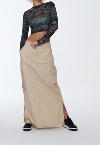 Sort langærmet crop top med blomstermotiv; beige lang cargo-nederdel med slids og lommer; parret med sorte sneakers.