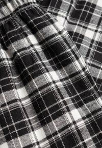 Schwarz-weiß kariertes Gewebe mit Schachbrettmuster. Weiche Textur mit markanten Quadraten und Linien, die durch kontrastierende Schattierungen und Tiefen hervorgehoben werden.