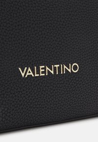 Sac en cuir noir avec une surface texturée, arborant un logo "VALENTINO" en or en relief bien visible sur le devant.