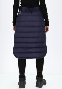 Tummansininen pufferskirt, jossa on vaakasuora toppauskuvio, vyöllinen vyötärö ja kaareva helma. Päällä mustat legginsit ja paksut, tukevat saappaat.