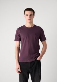 Tricou cu mânecă scurtă din bumbac de culoare violet închis, cu decolteu rotund și o etichetă logo mică în formă de pătrat pe piept. Croială standard.