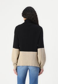 Pull en maille noir et beige avec col roulé, poignets côtelés et design en color-block. Texture douce, coupe décontractée et manches longues.