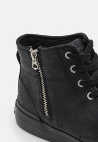 Svart fuskläder ankelsko med silverdragkedja, rund tå, metalögon och texturerad yta. Platt svart sula med subtila accenter.