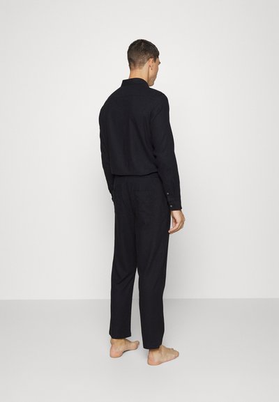 Conjunto de camisa e calças de linho preto, apresentando um corte descontraído e punhos com botões, mostrado por trás, com bolsos visíveis.