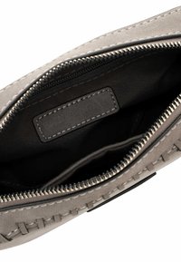 Intérieur d'un sac en cuir gris avec fermeture éclair, présentant une texture lisse, des accents cousus et une doublure en tissu noir avec une étiquette de marque.