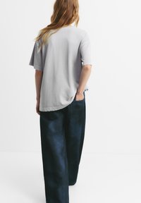 Tricou din bumbac gri, cu o croială lejeră și mâneci scurte, asortat cu pantaloni din denim cu picioare largi de culoare bleu închis. Textură netedă și design simplu.