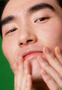 Nærbilde av et ansikt med glatt hud som glitrer lett. Hender berører kjevemuskulaturen. Bakgrunnen er en ensfarget grønn farge.